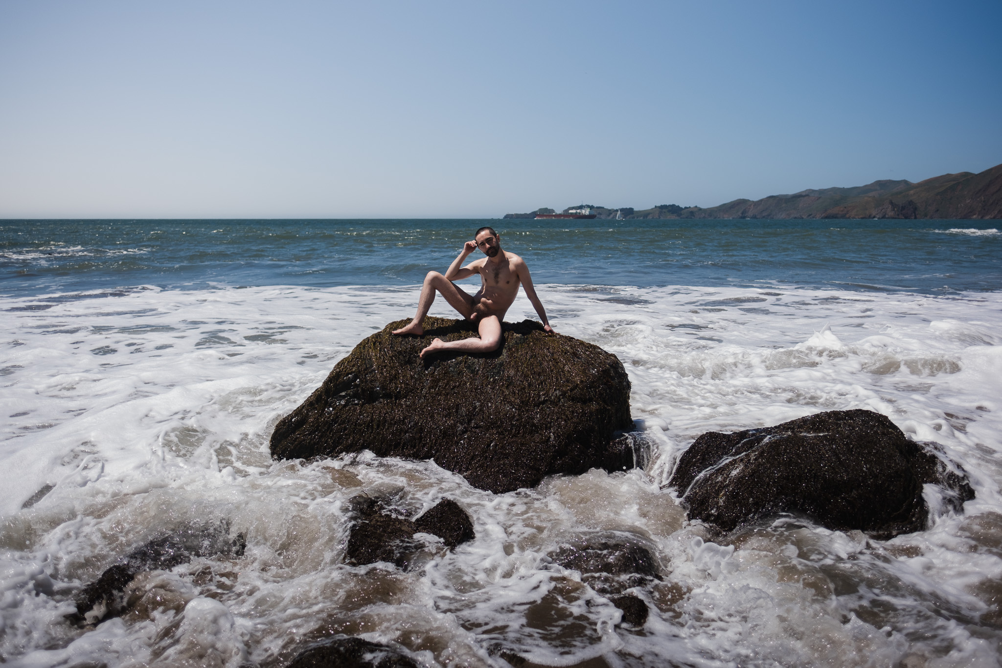 Nude self-portrait seated on a rock in the sea